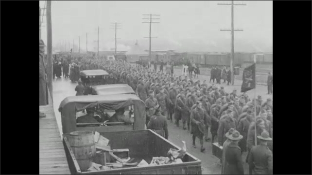 1910s: Train steams down tracks. Car drives down street. People walk around. Soldiers disembark from train. Soldiers march down street.