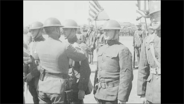 1910s: Officer pins medals on soldiers, men shake hands. 