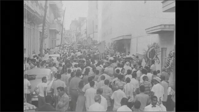 1960s Cuba: Utility plants in Cuba. Men work in plants. Men carry coffins through street.