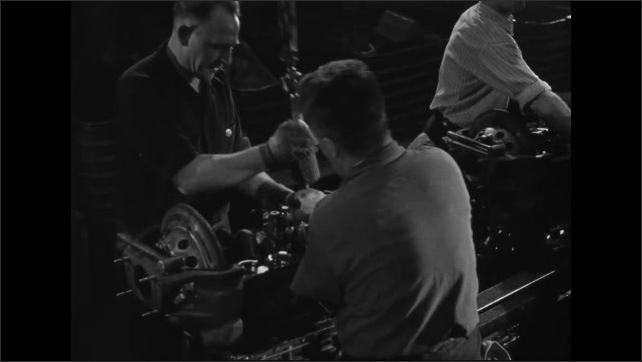 1950s: Men in automotive factory work on engines as they move down assembly line.