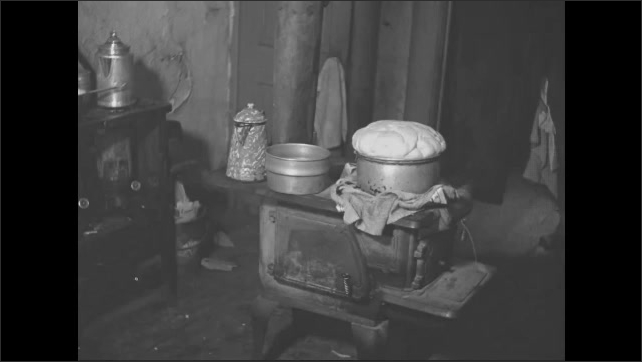 1950s: Interior home kitchen. Bread rising on wood-burning stove and duct pipe leading out from stove.