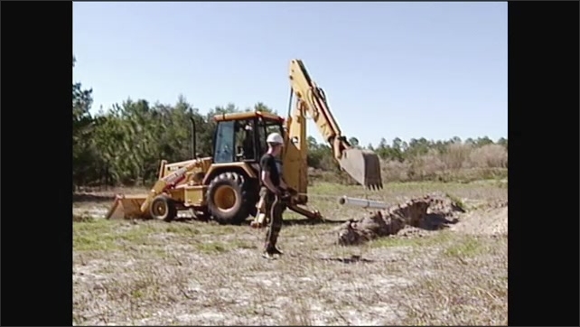 2000s: Excavator lifting pipe, man holds rope tied to pipe. Excavator ...