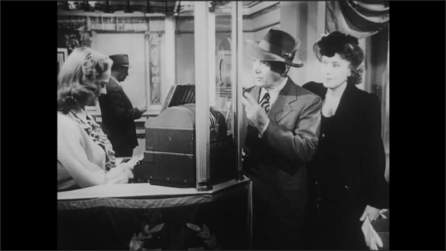 1940s: Theater.  Young woman sells tickets.  Sign reads "ALL STAR BOND RALLY."  Couple approaches ticket booth and speaks.  Couple walk away.