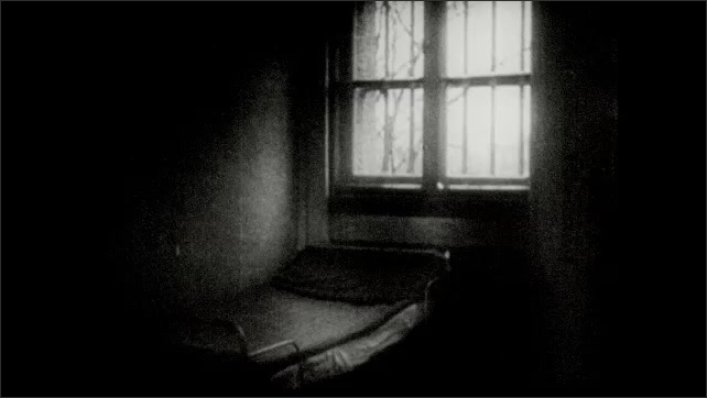 1930s: Adolf Hitler leaning out of window. Man in window. Open gate under archway. Prison exterior wall. Bed under window in jail cell. Book on table. Boats in canal. Person washing window.