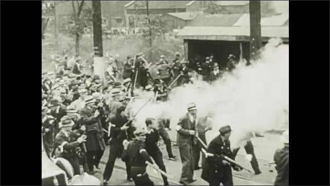 1910s: Strike busters fight with crowd of workers on street. Strike busters fire guns into crowd of workers near factory. Men carry unconscious man from demonstration.
