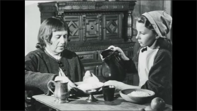 1940s: Boy holds out a plate and a woman pours milk into it. Boy starts to eat the mush. Girl pours milk into a man's plate. Children eat and drink quietly. Man drinks from a pewter mug.