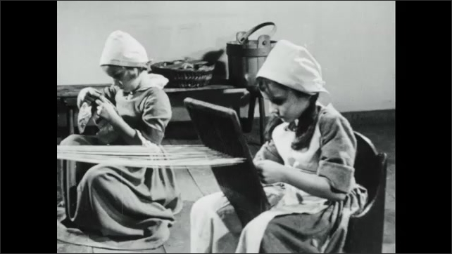 1940s: Fingers snap a stretched twine, leaving a chalk line on cloth. Women work on a quilt, while two girls work by the fireplace. One girl uses a hand loom. The other works on a needlepoint sampler.