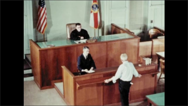 1960s: Defendant appears in court in Florida. Judge McCrary presides over courtroom. Defendant talks to judge at bar. Members of jury listen to defendant. Lady takes notes in court room. 