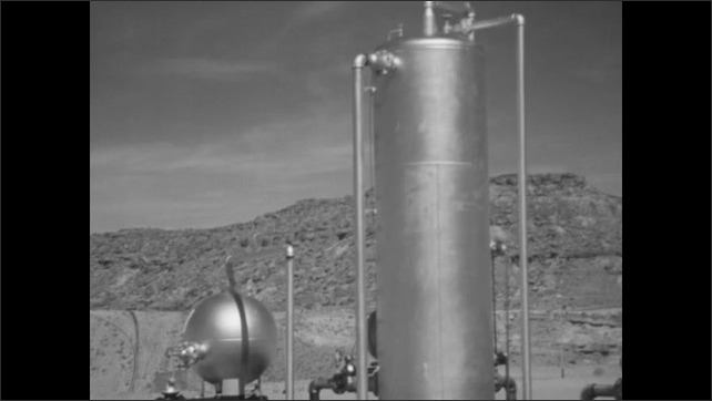 1950s: Several oil silos. Oil well pumps on hill, pipeline runs from well down hill. Oil pipeline processing units. Boy and sheriff stand looking at refinery.