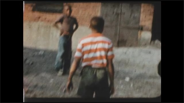 1960s: Boys toss ball and play in vacant lot behind city building.
