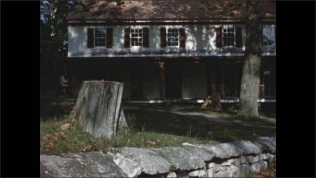 1770s: Exterior Colonial era building with stump in front and low stone wall. Large trees around house. 