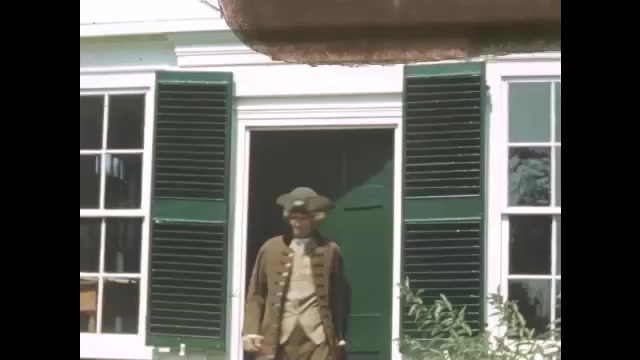 1700s: Colonial man exits home and buttons coat. Man walks on path away from house.