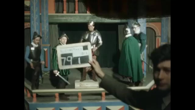 1500s: Low angle, men in period costume acting on stage. Clapboard. Man giving speech, men raise swords.  