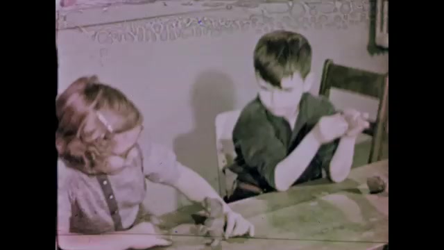 1950s: Classroom.  Little boy watches girl working with clay.  Clay animal.  Boy raises lump of clay over head.  