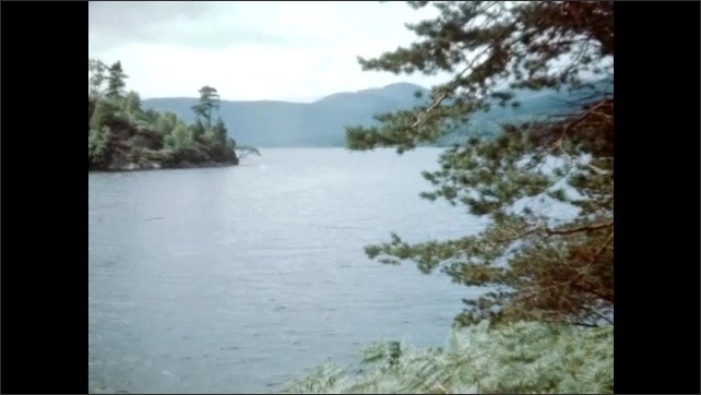 1940s: Trees stand near the waters of Loch Katrine in Scotland. Water ripples on mountain valley lake. Mountain overlooks tree-filled valley