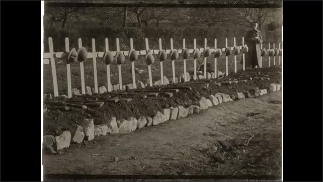 1910s: Row of graves with helmets on markers. Soldiers stand together, posing.