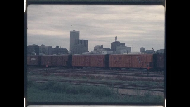 1970s: Train in rail yard, city in background. Close up of sunflowers, zoom out to train in rail yard. 