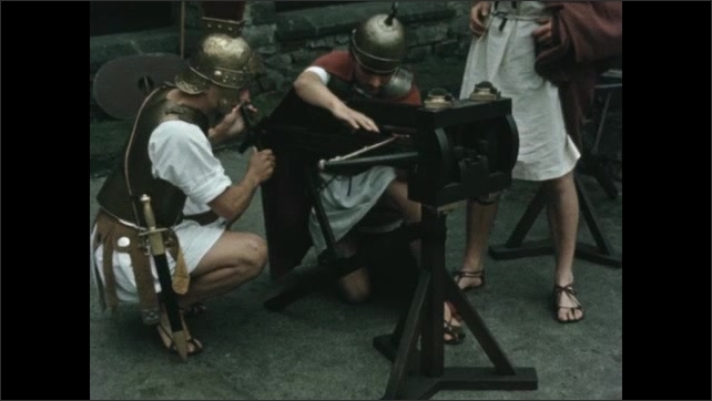 Decade: Roman soldiers set up ballista catapult. Roman soldiers in uniform. Roman man with knife. 