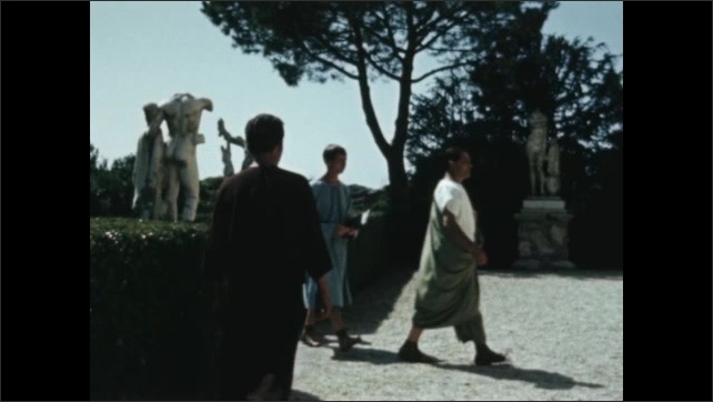 Decade: Roman villa exterior. Men talk on steps of Roman villa. Men in Roman age gardens. Man in toga. Stone statues in garden courtyard.