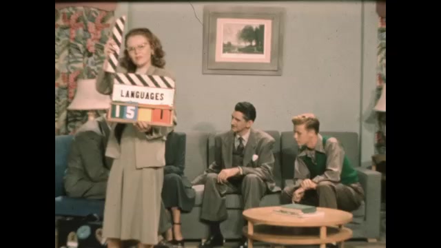 1940s: Clapperboard. Four people have meeting in office lounge. Man gets up and opens stickers briefcase. Man takes papers out and hands them to woman, who looks and passes to man beside her.