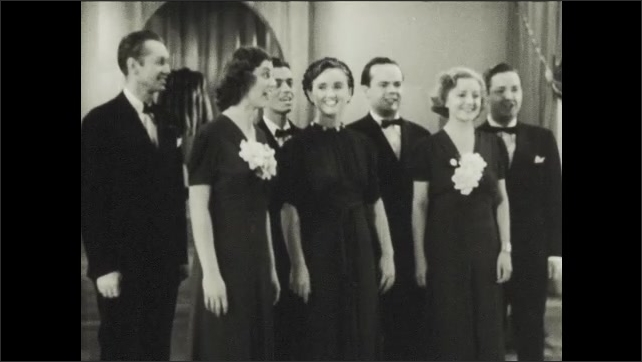 1930s: Group of three women and four men stand together on floor at performance, singing together.