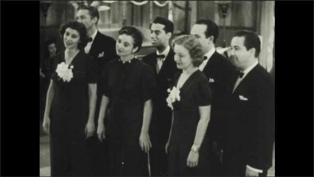 1930s: Group of three women and four men stand together on floor at performance, singing together.