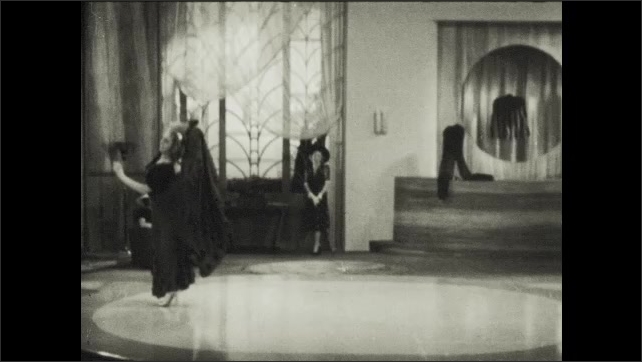 1930s: Man stands on floor at performance talking to audience. Woman comes onto floor and dances while contorting her body.
