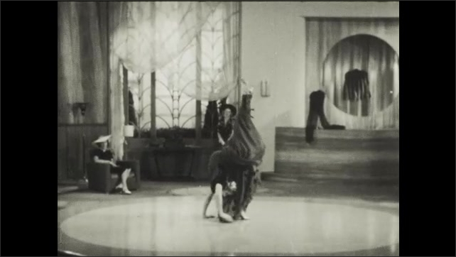 1930s: Woman on floor at performance dances, doing acrobats and contortions, walks on hands. Woman stops. Audience claps. Man talks place on floor, talking to audience.
