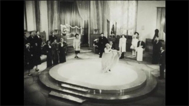 1930s: Woman walks on to floor of performance where fur coat, coat is removed, man joins woman and they begin to sing and dance together for audience.