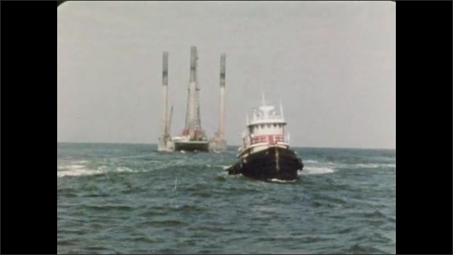 1960s: UNITED STATES: mobile rig at sea. Boat tows rig out to sea. Tugs ...