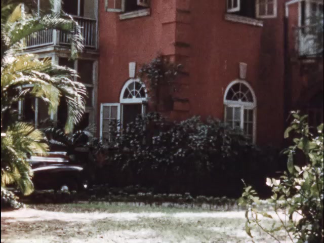 1950s: Car drives up to house. People exit car, walk under archway. 