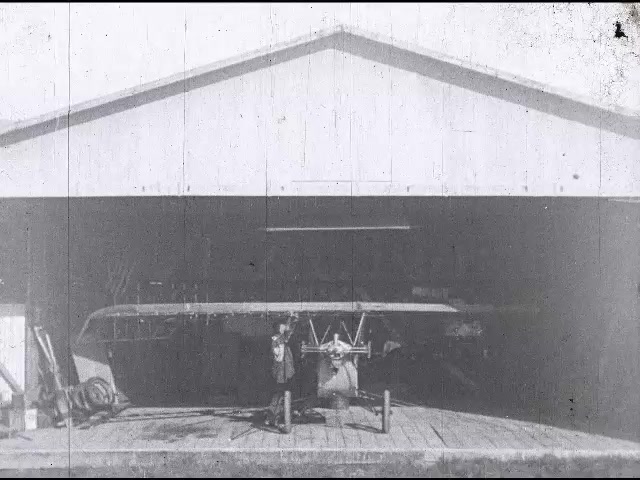 1920s: Garage, man in overalls inspects, walks around, works on glider, attaches support to wings, spins glider around, sets tail down. 