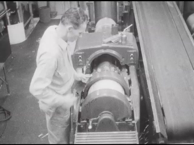 1950s: Man moving machine parts. Plate sliding on conveyor belt. Mna puts plate on roller in printing press, presses button. 