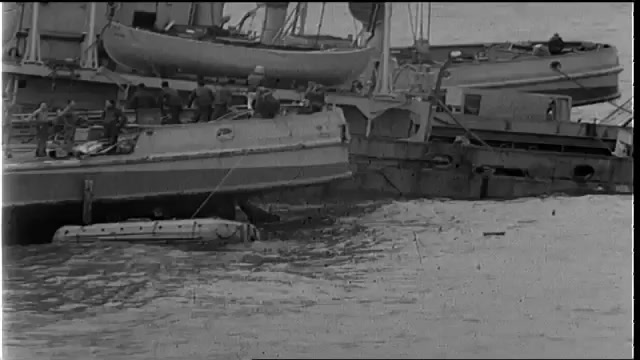 1940s: Boat next to partially submerged ship.  Land.  Debris floats in water.