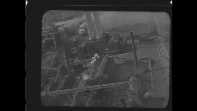 1920s: Looking down on factory buildings on large complex from sky above. Stream and smoke rise from factory buildings.