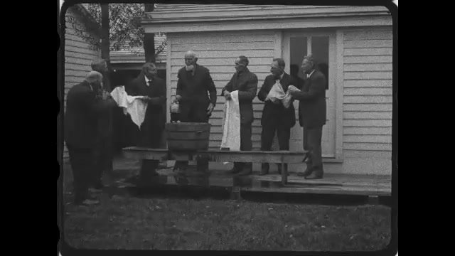 1920s: Men wash themselves in water basin on porch of house, men drink from jug, man brings out large jug and drinks from that.