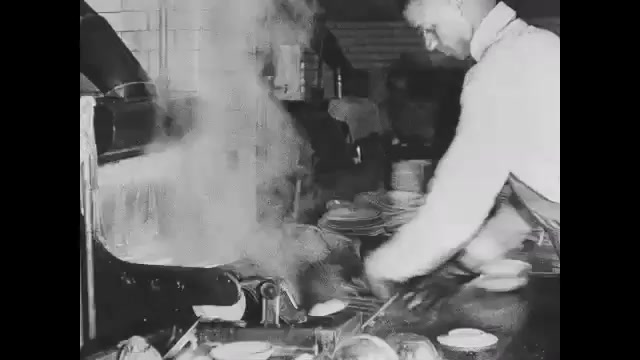 1910s: Person in restaurant kitchen pulls clean dishes from dishwasher. Pile of clean dishes. Intertitle card. Man pours cream into pot to make ice cream.