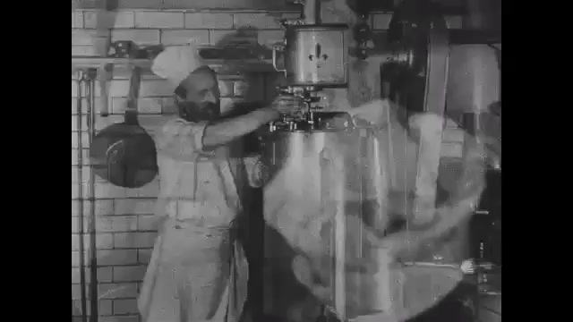 1910s: Man in restaurant kitchen wipes down ice cream making machine. Ice cream pours out of spout in machine into cup. Man eats ice cream. Intertitles. Women sew clothes in garment shop.