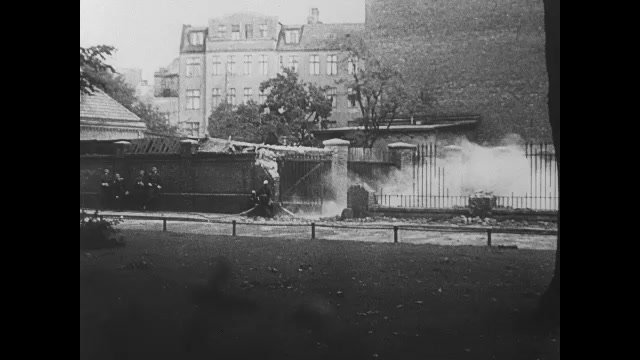 1930s Germany: Soldiers spraying hose at building. Soldiers fire gun. Fire outside building. Soldiers running. Pan across damaged building. Shots of building. Car pulls up to officials on street.