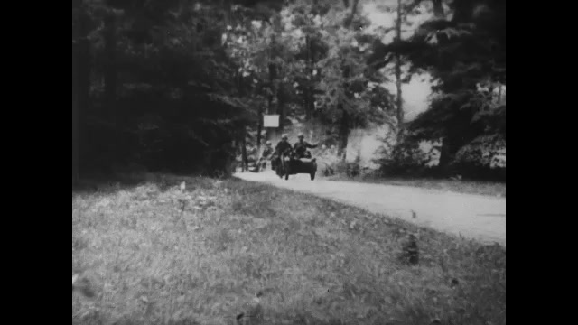 1930s Germany: Nazi soldiers drive motorcycles off of road. Motorcycles driving on road. Soldiers hide on ground. Pan, soldiers riding horses. Title card. 