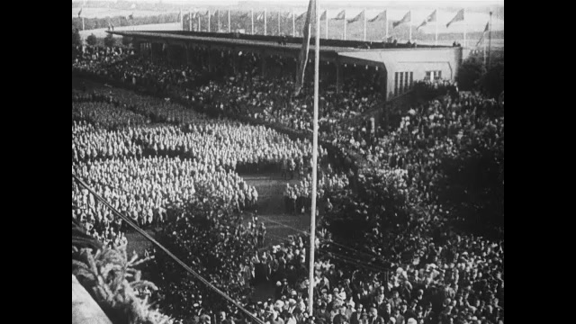 1930s Germany: Crowded stadium.  Hitler yells and gestures.  Soldiers stand in rows on grass.