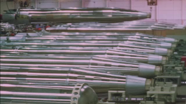 1960s: ICBM Missile body and base is lifted and moved above a long row ...