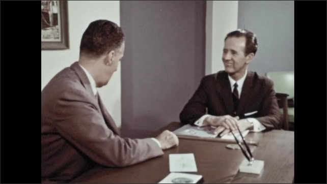 1960s: Man enters bank. Man stands and shakes man's hand. Men sit and speak. Man hands paper to man. Man writes on paper.