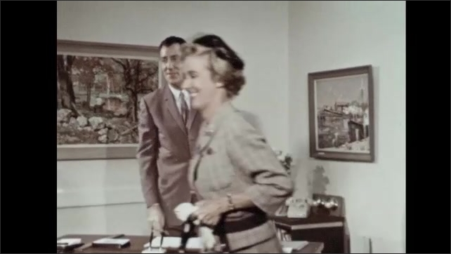 1960s: Woman looks at papers and speaks. Woman puts papers in purse and stands. Man and woman shake hands. Man speaks.