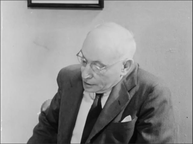 1950s: Man in glasses speaking, looking over shoulder.