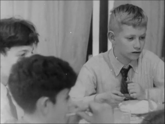 1950s: Boys sitting around table, talking. Boy talking, playing with spoon.