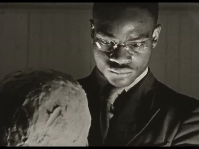 1940s: Intertitles. Man sculpts person's head. Woman sculpts persons head, talks to man pointing to shape of his head.