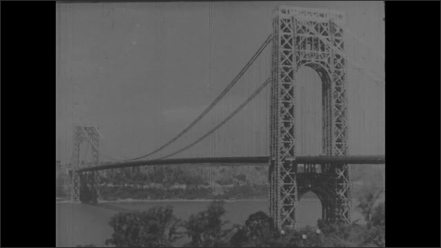 1930s: Intertitle. View of George Washington Bridge. Cars driving onto bridge. Sign for Holland Tunnel.