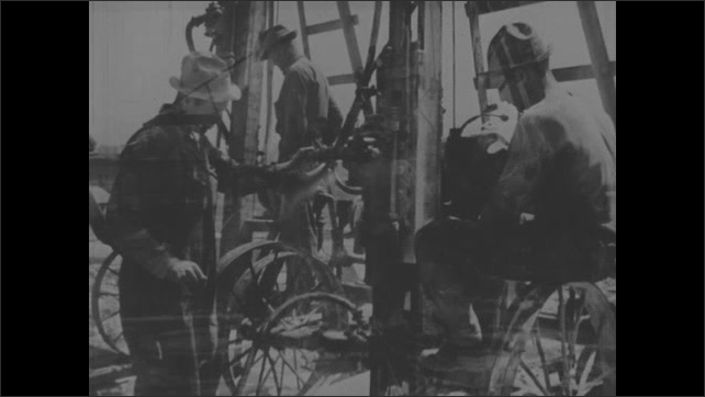 1930s: Man looks through surveying equipment. Man in workshop. Metal bars in furnace. Men drilling on construction site. Shots of gears turning.