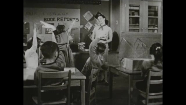 1950s: Children putting up their hands in class. Teacher lecturing class, children put their hands up. Children working on large drawing.